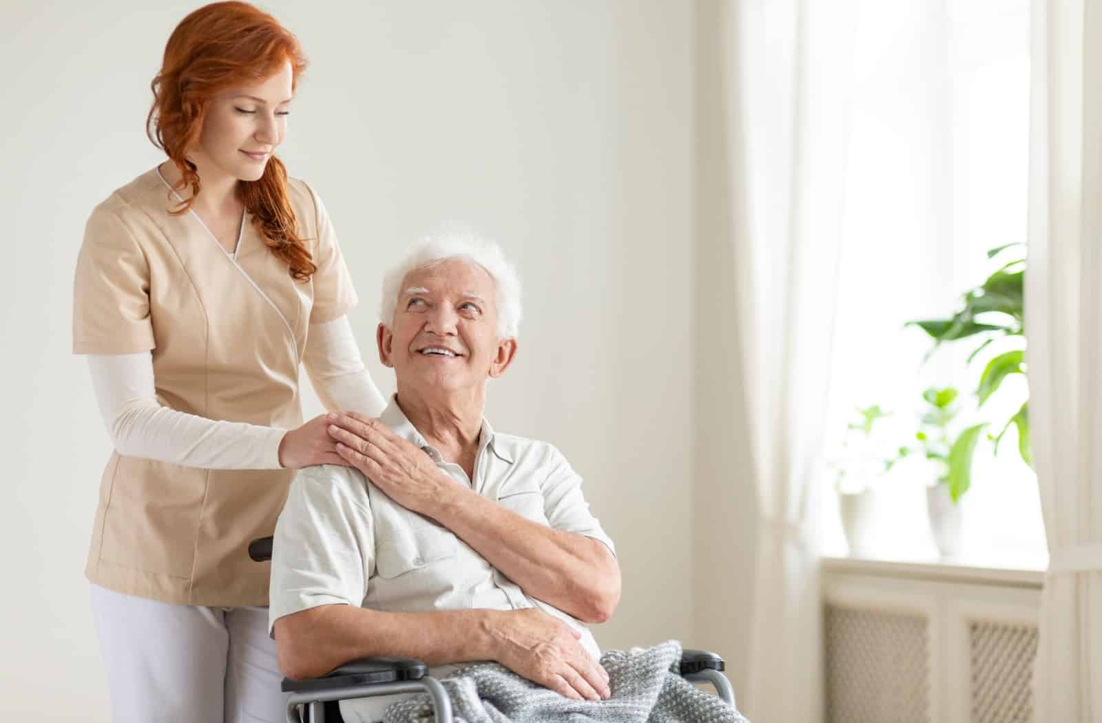 A senior man in a wheelchair being assisted by a caregiver.
