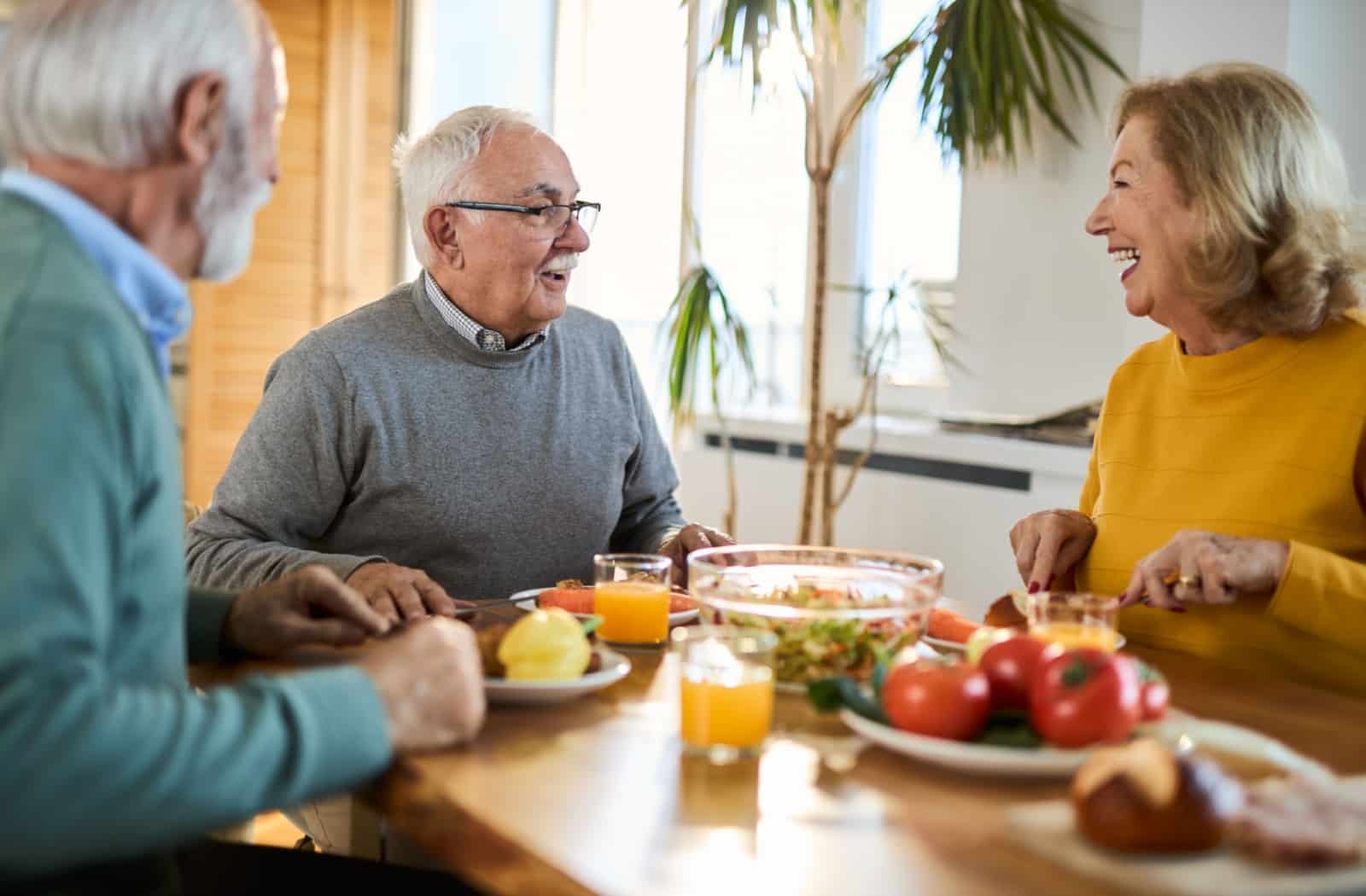 Three seniors laugh over a nutritious meal together in assisted living, enjoying company with like-minded individuals